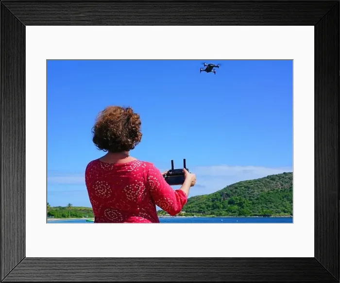 Framed Print : ST KITTS, ST KITTS AND NEVIS -21 NOV 2018- A woman taking pictures with a drone camera over the Caribbean Sea in Framed Print : ST KITTS, ST KITTS AND NEVIS -21 NOV 2018- A woman taking pictures with a drone camera over the Caribbean Sea in