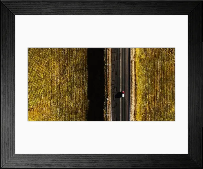 Framed Print : Drone view of moving red car on country side road with beautiful green field around