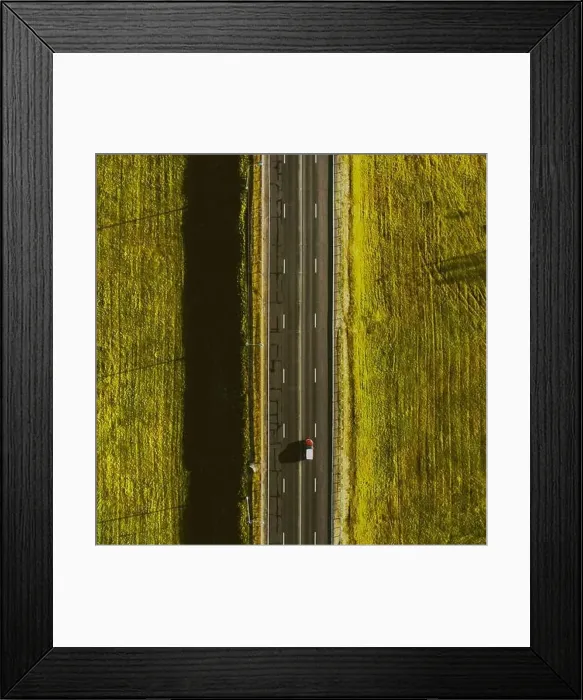 Framed Print : Drone view of moving red car on country side road with beautiful green field around