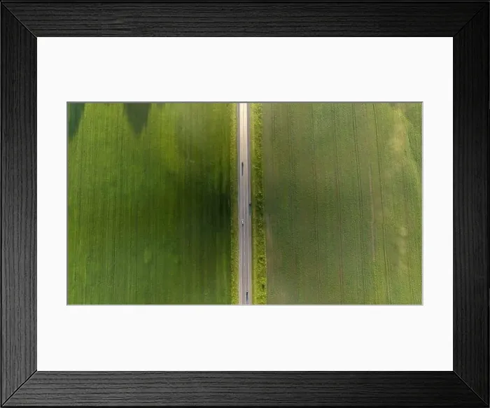 Framed Print : Aerial top view of a landscape while traveling by car on an asphalt highway in the middle of a green agricultural field Framed Print : Aerial top view of a landscape while traveling by car on an asphalt highway in the middle of a green agricultural field