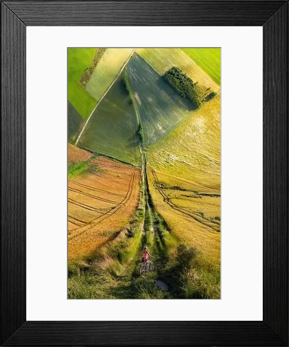Framed Print : Cyclist on road toward square field amongst meadows in warp perspective, Mazury Poland Framed Print : Cyclist on road toward square field amongst meadows in warp perspective, Mazury Poland