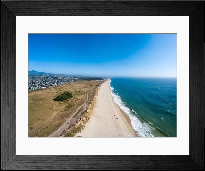 Framed Print : Aerial Of beach blue waves clashing on the shore on a afternoon with city and mountains hazy horizon Framed Print : Aerial Of beach blue waves clashing on the shore on a afternoon with city and mountains hazy horizon