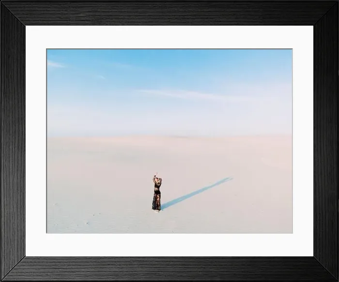 Framed Print : Woman in lace black dress stands in desert and casts a shadow on white sand. View from drone Framed Print : Woman in lace black dress stands in desert and casts a shadow on white sand. View from drone