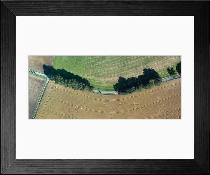 Framed Print : Aerial view of a green agricultural field with a rural road passing through it. Summer time, sunny day in landscape Framed Print : Aerial view of a green agricultural field with a rural road passing through it. Summer time, sunny day in landscape