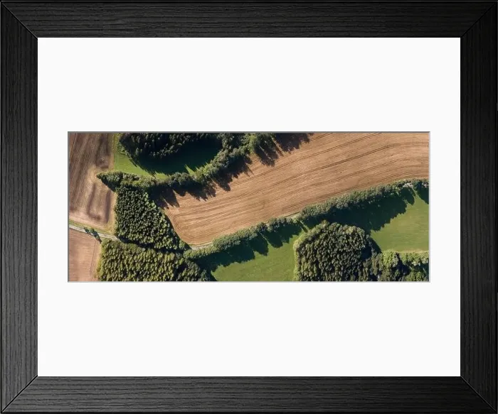 Framed Print : Aerial view of a green agricultural field with a rural road passing through it. Summer time, sunny day in landscape Framed Print : Aerial view of a green agricultural field with a rural road passing through it. Summer time, sunny day in landscape