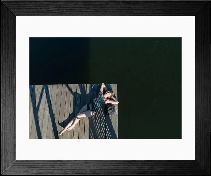 Framed Print : Top view of beautiful Woman in black swimsuit and hat lying down on wooden pier of lake on clear blue sky Framed Print : Top view of beautiful Woman in black swimsuit and hat lying down on wooden pier of lake on clear blue sky