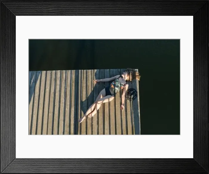 Framed Print : Top view of beautiful Woman in black swimsuit and hat lying down on wooden pier of lake on clear blue sky Framed Print : Top view of beautiful Woman in black swimsuit and hat lying down on wooden pier of lake on clear blue sky