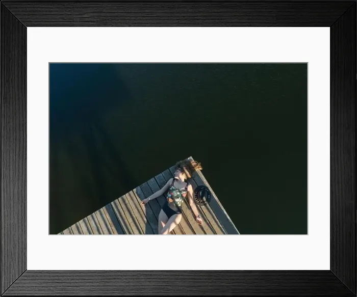 Framed Print : Top view of beautiful Woman in black swimsuit and hat lying down on wooden pier of lake on clear blue sky Framed Print : Top view of beautiful Woman in black swimsuit and hat lying down on wooden pier of lake on clear blue sky