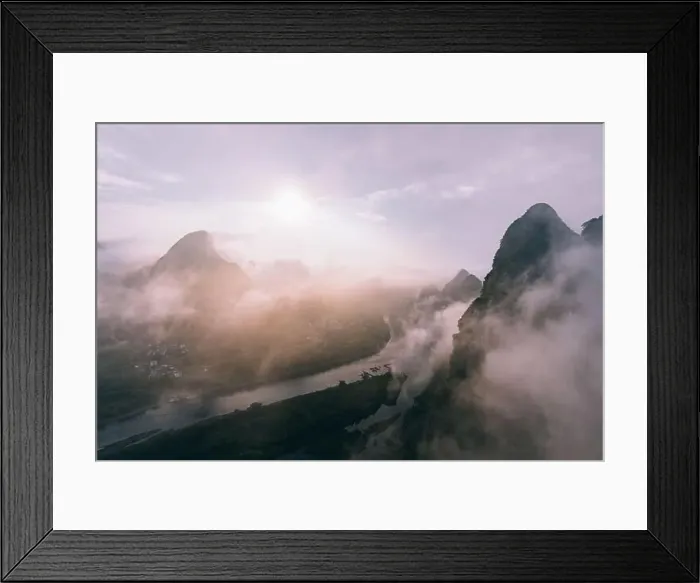 Framed Print : Drone view of calm river and rocky dark mountains in morning mist with flowing clouds under bright sky and sun Framed Print : Drone view of calm river and rocky dark mountains in morning mist with flowing clouds under bright sky and sun