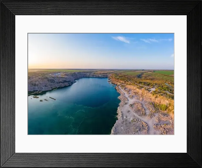 Framed Print : Old flooded stone quarry with large stones in the evening warm bright light covered with small dry plants in