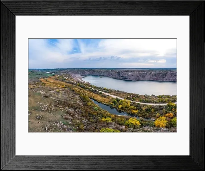 Framed Print : Old flooded stone quarry with large stones in the evening warm bright light covered with small dry plants in