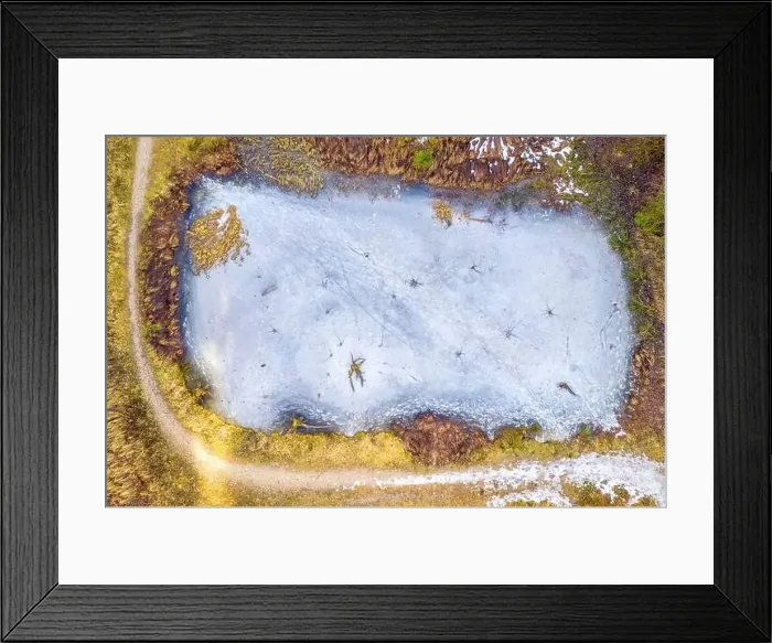 Framed Print : Top view of frozen lake covered with blue ice and surrounded by a snowy path at a beautiful winter landscape Framed Print : Top view of frozen lake covered with blue ice and surrounded by a snowy path at a beautiful winter landscape