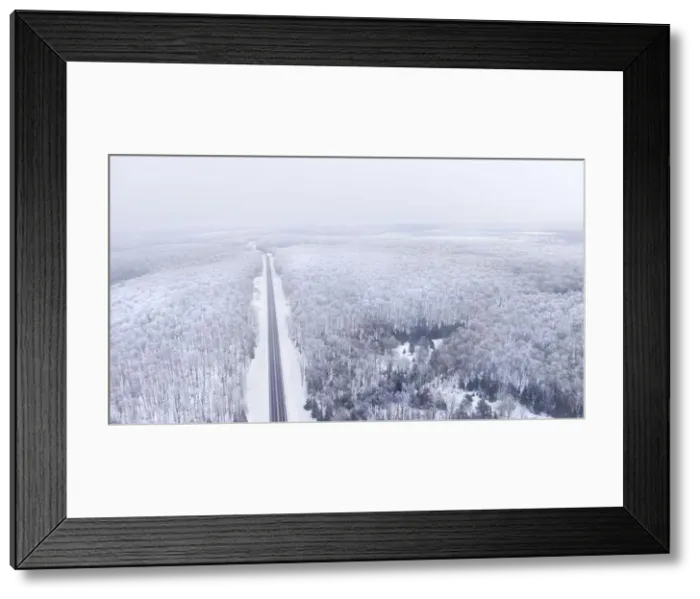 Framed Print : Aerial view of a road cutting through a snowy forest on a cloudy day Framed Print : Aerial view of a road cutting through a snowy forest on a cloudy day