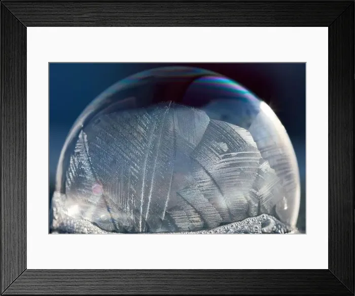 Framed Print : Close-up macro of a frozen soap bubble with abstract pattern in winter sunlight, isolated on blue Framed Print : Close-up macro of a frozen soap bubble with abstract pattern in winter sunlight, isolated on blue