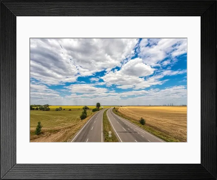 Framed Print : highway passing through the fields against a blue sky with beautiful white clouds Framed Print : highway passing through the fields against a blue sky with beautiful white clouds