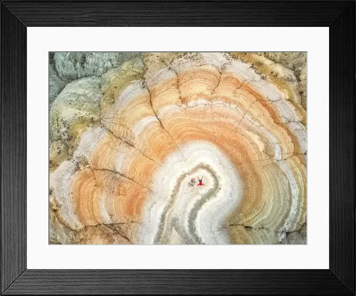 Framed Print : Aerial drone shot of man lying with his bicycle on the top of surreal striped red and white desert mountain Framed Print : Aerial drone shot of man lying with his bicycle on the top of surreal striped red and white desert mountain