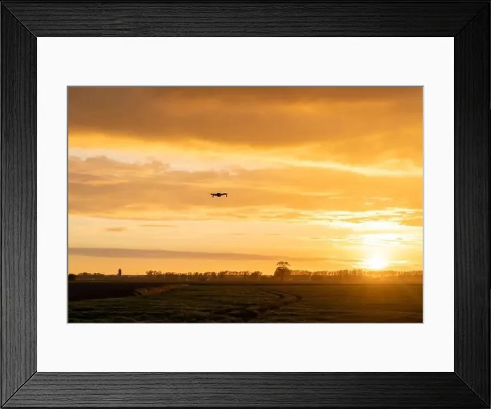 Framed Print : A drone flying over green springtime meadows with a colorful orange sunset sky behind Framed Print : A drone flying over green springtime meadows with a colorful orange sunset sky behind