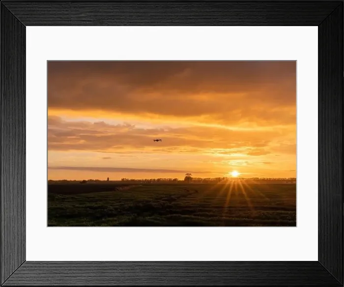 Framed Print : A drone flying over green springtime meadows with a colorful orange sunset sky behind Framed Print : A drone flying over green springtime meadows with a colorful orange sunset sky behind