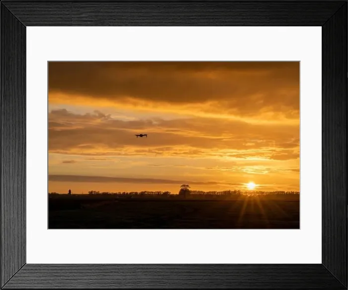 Framed Print : A drone flying over green springtime meadows with a colorful orange sunset sky behind Framed Print : A drone flying over green springtime meadows with a colorful orange sunset sky behind