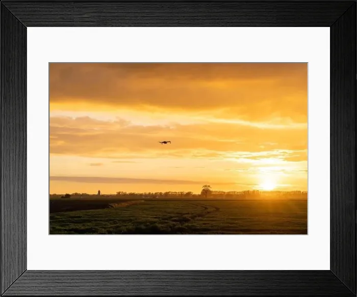 Framed Print : A drone flying over green springtime meadows with a colorful orange sunset sky behind Framed Print : A drone flying over green springtime meadows with a colorful orange sunset sky behind