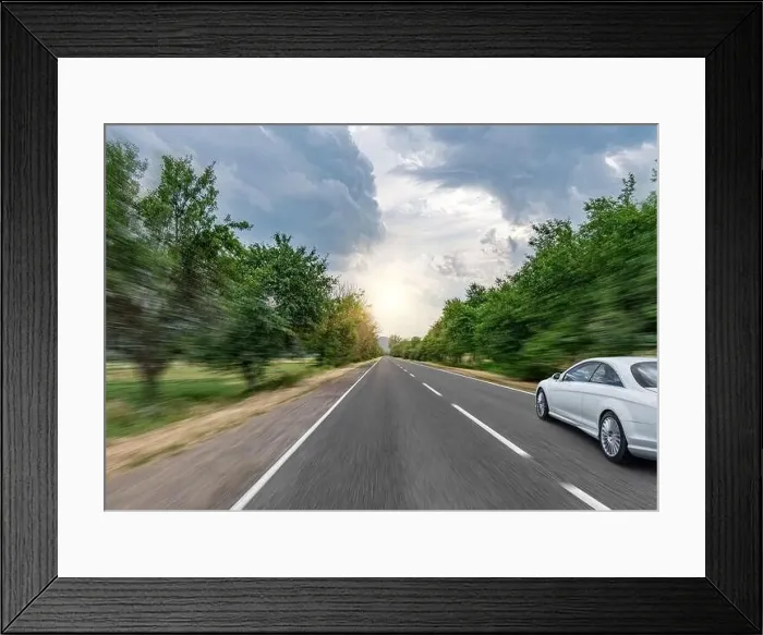 Framed Print : White car drives down the road through the forest along the highway Framed Print : White car drives down the road through the forest along the highway