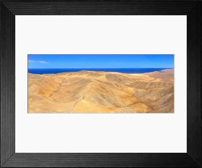 Framed Print : Aerial view of empty road crossing the desert mountains towards the blue Atlantic Ocean Framed Print : Aerial view of empty road crossing the desert mountains towards the blue Atlantic Ocean