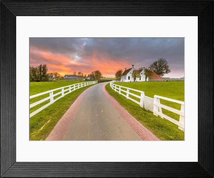 Framed Print : Dutch Countryside landscape with historical houses in evening along a curved road with white fence in the country Framed Print : Dutch Countryside landscape with historical houses in evening along a curved road with white fence in the country