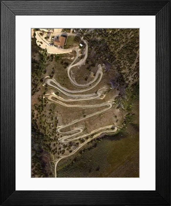 Framed Print : Aerial view from a drone flying above a winding curved dirt road on mountainside