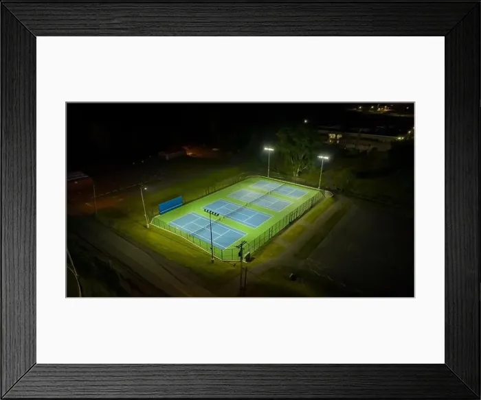Framed Print : Evening aerial video of outdoor blue tennis courts with pickleball lines with lights turned on Framed Print : Evening aerial video of outdoor blue tennis courts with pickleball lines with lights turned on
