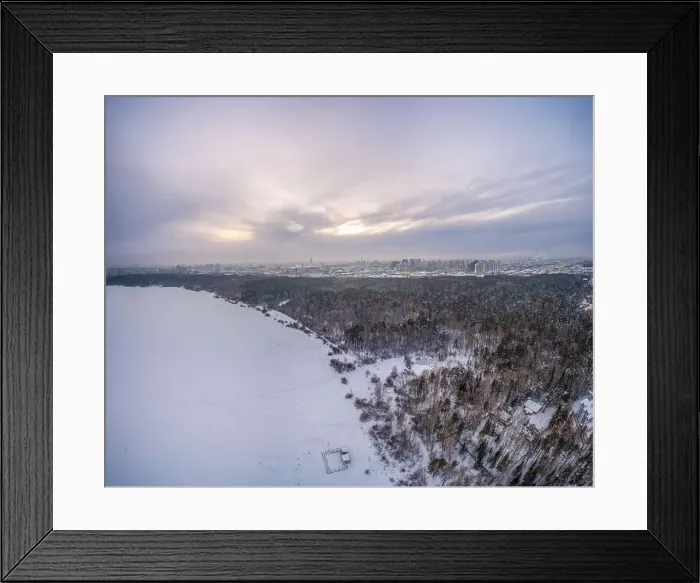 Framed Print : Snow-covered forest on lake shore with ice at sunset and the city on horizon Framed Print : Snow-covered forest on lake shore with ice at sunset and the city on horizon