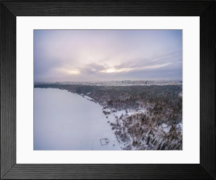 Framed Print : Snow-covered forest on lake shore with ice at sunset and the city on horizon Framed Print : Snow-covered forest on lake shore with ice at sunset and the city on horizon
