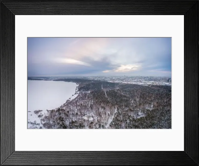 Framed Print : Snow-covered forest on lake shore with ice at sunset and the city on horizon Framed Print : Snow-covered forest on lake shore with ice at sunset and the city on horizon