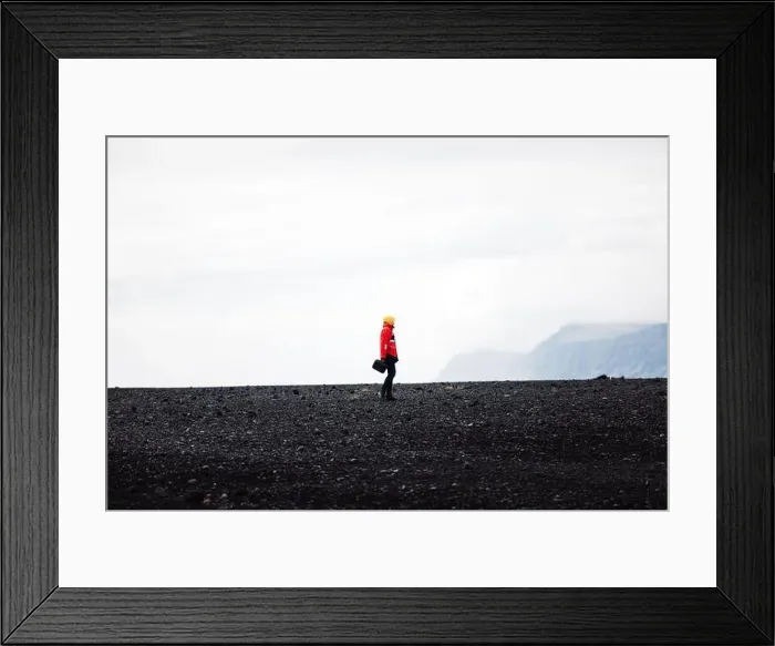 Framed Print : Traveler in a red jacket standing on a black sand beach in Iceland Framed Print : Traveler in a red jacket standing on a black sand beach in Iceland