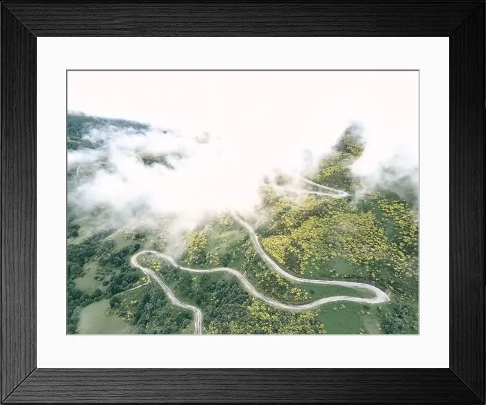 Framed Print : image taken with a drone of the long road with many curves under the fog on the slope of the green mountain between Framed Print : image taken with a drone of the long road with many curves under the fog on the slope of the green mountain between