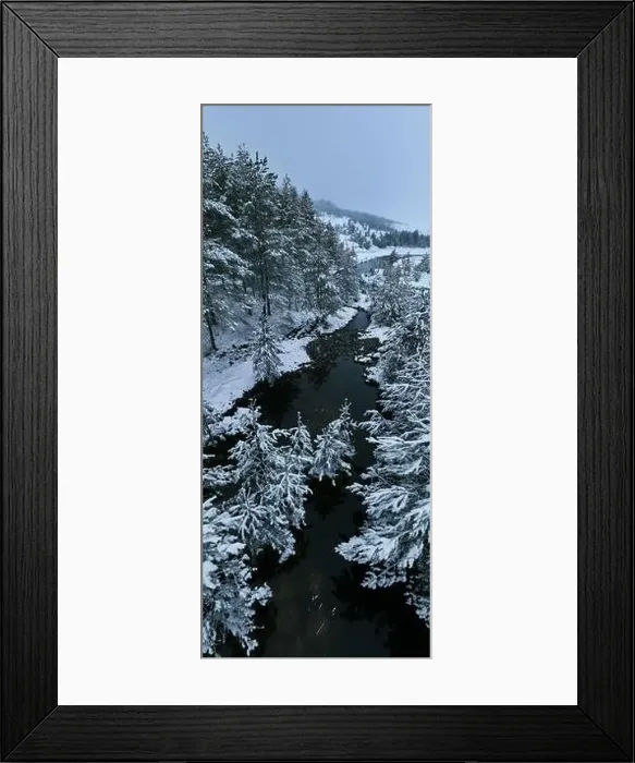 Framed Print : An aerial view of a frozen river flowing through snow-covered forests on a cloudy sunset sky background