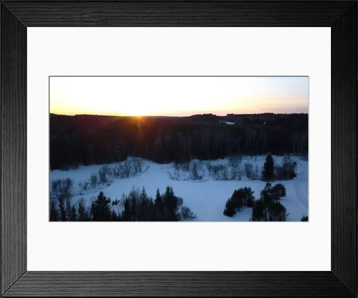 Framed Print : Aerial view of a snowmobile driving along pine tree forest. Clip. Sunset sky and rural snow covered road