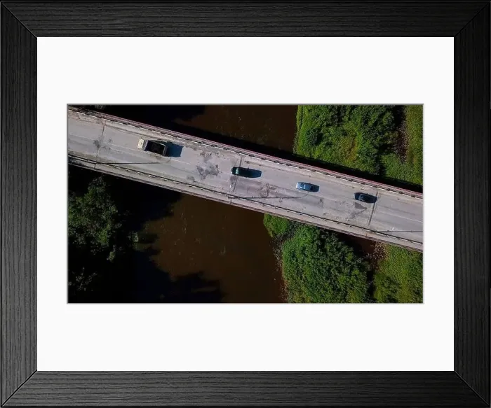 Framed Print : Aerial top view of a narrow bridge above brown dirty river. Clip. Green shores with bushes and driving cars Framed Print : Aerial top view of a narrow bridge above brown dirty river. Clip. Green shores with bushes and driving cars