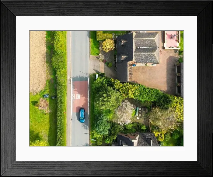 Framed Print : Drone top down view of a Slow road markings seen on a dangerous rural English road. A single car passes at speed Framed Print : Drone top down view of a Slow road markings seen on a dangerous rural English road. A single car passes at speed