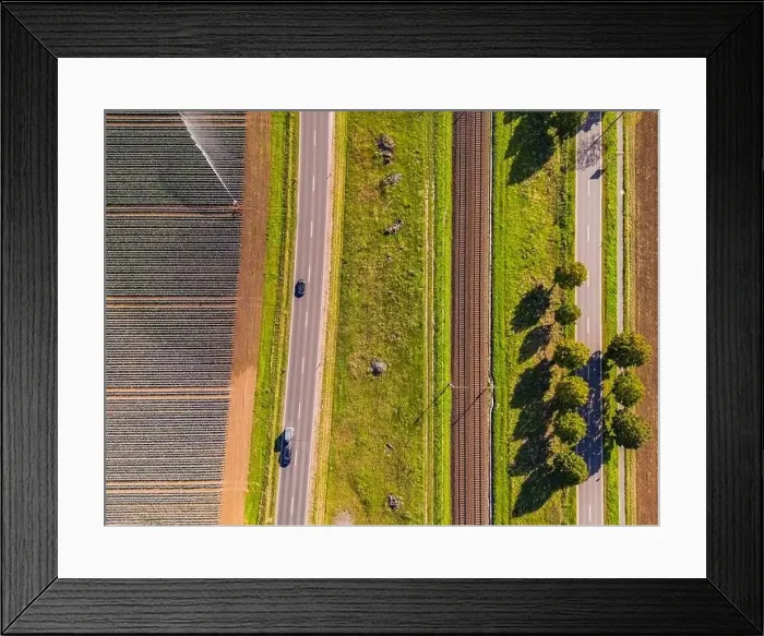 Framed Print : A railroad line with two tracks next to two roads and fields next to agricultural fields Framed Print : A railroad line with two tracks next to two roads and fields next to agricultural fields