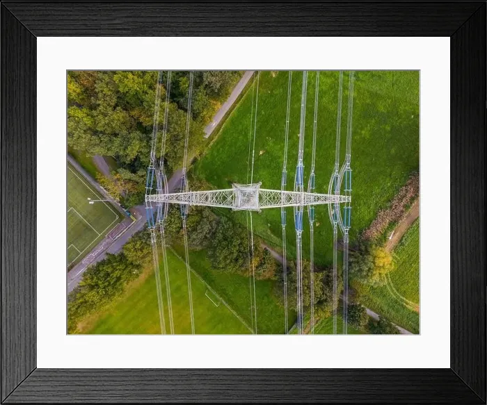 Framed Print : High voltage pylon with power lines between nature and sports field photographed directly from above with drone Framed Print : High voltage pylon with power lines between nature and sports field photographed directly from above with drone