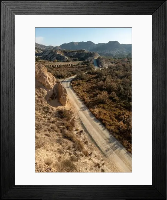 Framed Print : Dirt road in arid desert landscape with distant cliffs and morning sunlight Framed Print : Dirt road in arid desert landscape with distant cliffs and morning sunlight