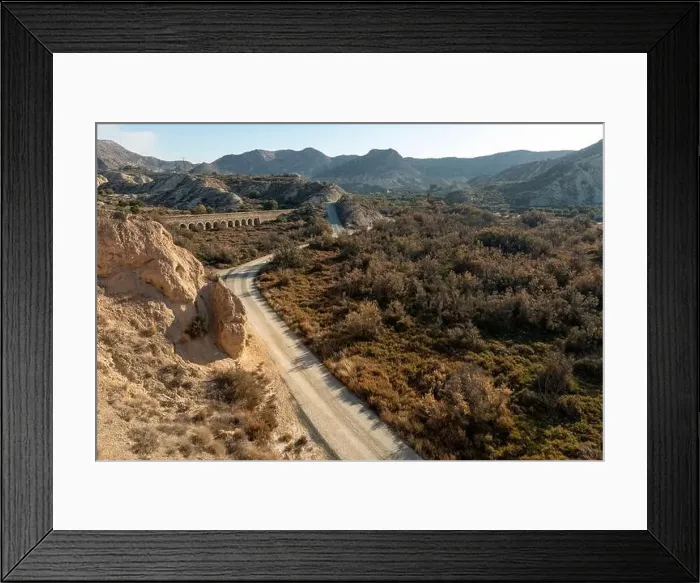 Framed Print : Dirt road in arid desert landscape with distant cliffs and morning sunlight Framed Print : Dirt road in arid desert landscape with distant cliffs and morning sunlight