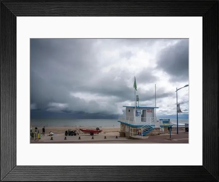 Framed Print : Langrune-Sur-Mer, France - 07 26 2023: View of the sea, the jetty and people walking on the beach with a cloudy sky Framed Print : Langrune-Sur-Mer, France - 07 26 2023: View of the sea, the jetty and people walking on the beach with a cloudy sky