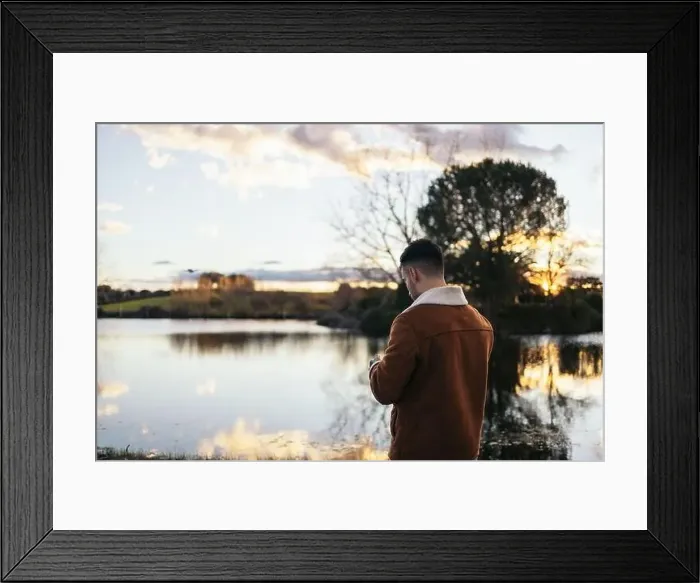 Framed Print : Young man using a drone near a lake to record and photograph the landscape Framed Print : Young man using a drone near a lake to record and photograph the landscape