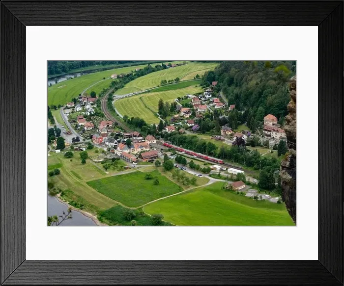 Framed Print : A train is traveling through a small town with houses and a river in the background Framed Print : A train is traveling through a small town with houses and a river in the background