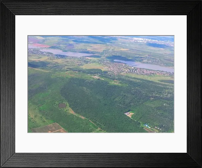 Framed Print : Aerial view of a green forest with a town in the distance Framed Print : Aerial view of a green forest with a town in the distance
