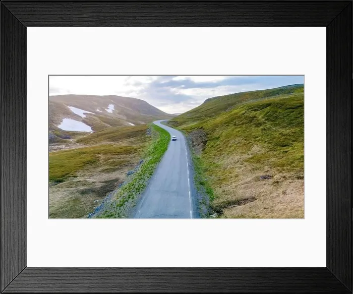 Framed Print : A single car drives along a winding road through a green Framed Print : A single car drives along a winding road through a green