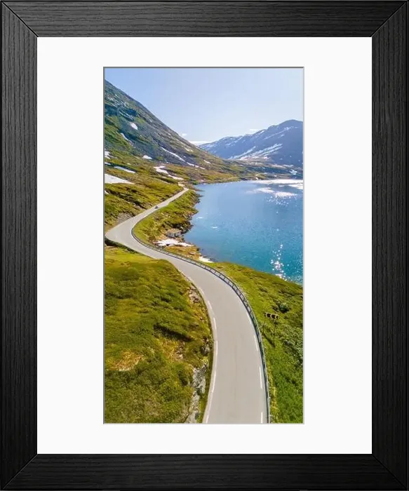 Framed Print : An aerial view of a winding road snaking through green mountains and a glistening blue lake in Norway Framed Print : An aerial view of a winding road snaking through green mountains and a glistening blue lake in Norway