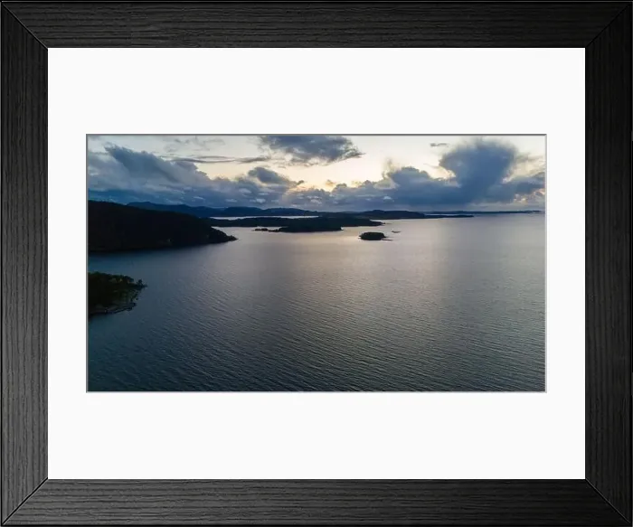Framed Print : A serene aerial view of a large fjord with small islands and distant hills under a cloudy sky at dusk Framed Print : A serene aerial view of a large fjord with small islands and distant hills under a cloudy sky at dusk