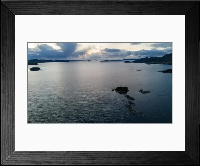 Framed Print : Aerial view of a calm fjord with small rocky islands and distant mountains under a cloudy sky Framed Print : Aerial view of a calm fjord with small rocky islands and distant mountains under a cloudy sky